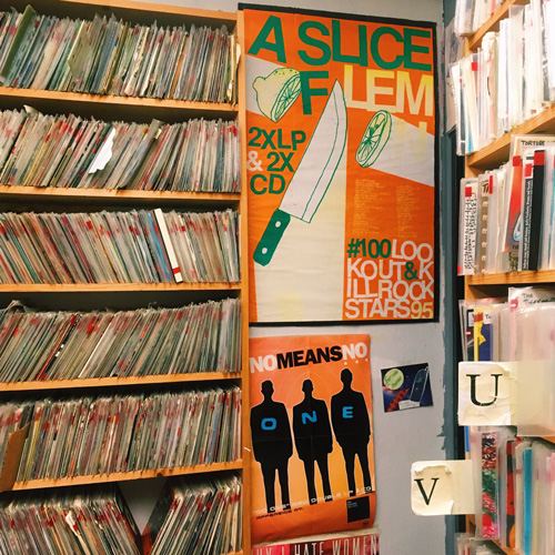 A photo of a radio station, showing stacks of records and several posters for musicians on the walls.