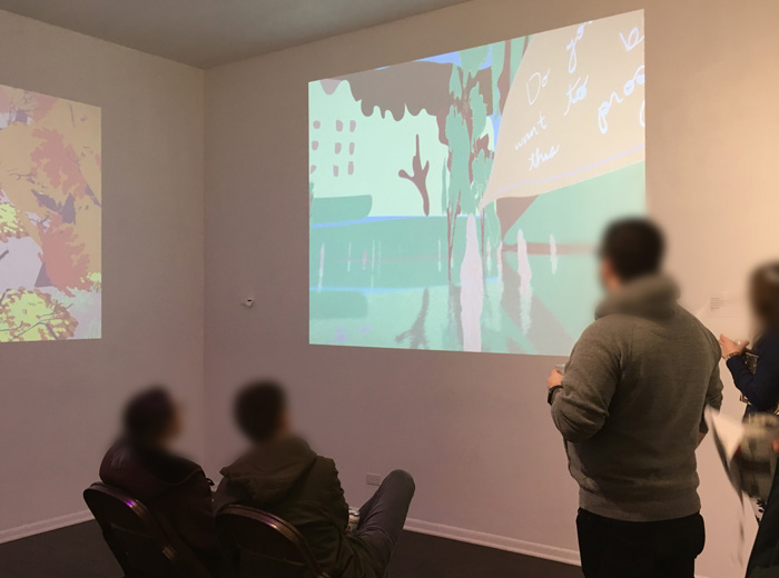 A photo of several people playing or looking at a game being projected onto a white wall. Their faces are blurred out as they look at the projection. Another projection is visible on the adjacent wall.