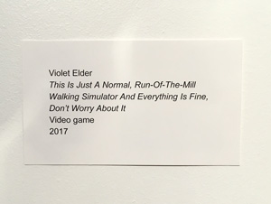 A photo of a display placard reading Violet Elder, This Is Just A Normal, Run-Of-The-Mill Walking Simulator And Everything Is Fine, Don't Worry About It. Video Game. 2017.