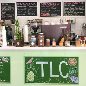 A photo of a cafe's front counter, chalkboard menu featuring drawings of fruit and reading TLC.
